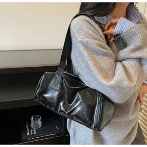 Borsa Boston in pelle verniciata nera lucida indossata come borsa a spalla retrò