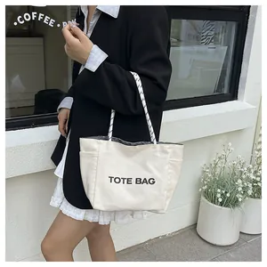 Detail of white canvas tote bag with black lettering and woven rope handles on a model