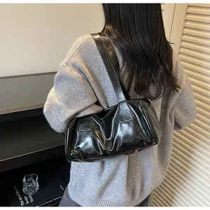 Dettaglio di una borsa a spalla nera lucida con texture in pelle verniciata e tracolla larga