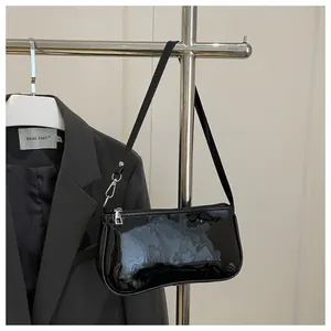Close-up of black patent leather baguette bag with silver zipper on a metal hanger