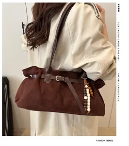 Detail of dark brown suede shoulder bag with leather strap and wooden bead charm
