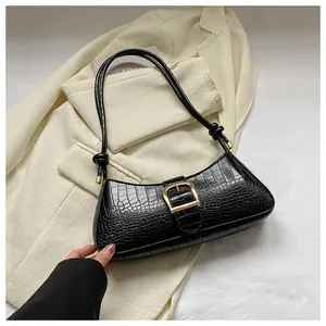 Detail of black faux crocodile leather baguette bag with a large gold buckle and knot strap