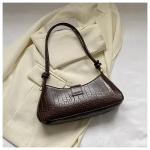 Macro shot of dark brown crocodile pattern bag on a beige textured blazer