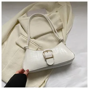 Detail of white crocodile embossed baguette bag with gold buckle on beige blazer