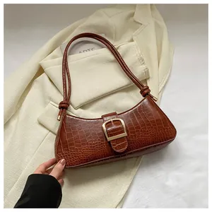 Detail of dark brown croc-embossed leather underarm bag with gold buckle and knot strap