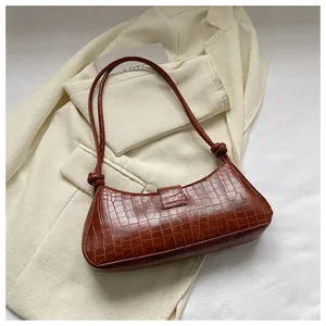 Detailed macro view of dark brown faux-crocodile texture and knotted strap on baguette bag