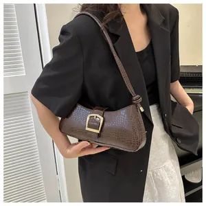 Detail of dark brown crocodile pattern handbag with golden buckle on model