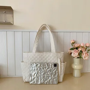 Close-up of cream quilted tote bag with side pockets and silver tablet for size scale