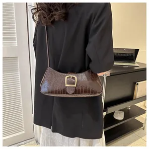 Detail shot of a dark brown crocodile pattern baguette bag with gold buckle on shoulder