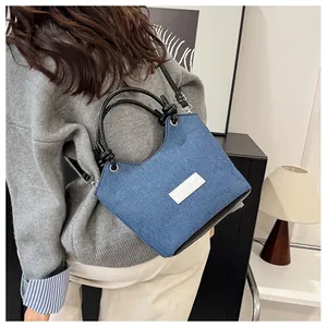 Détail d'un sac bandoulière en denim bleu et cuir noir porté par un mannequin en intérieur