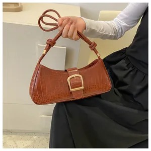 Detail of brown crocodile pattern underarm bag with gold buckle and knot strap