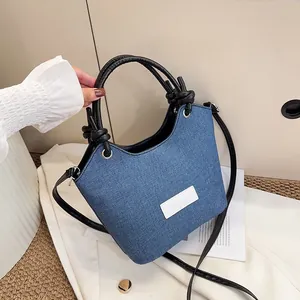 Détail du sac cabas en denim bleu avec poignées en cuir nouées et écusson mode