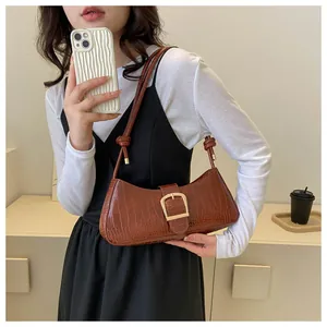 Detail of brown crocodile pattern baguette bag featuring gold buckle and knotted shoulder strap
