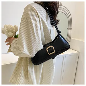 Detail of black baguette bag with crocodile texture and gold square buckle on a model