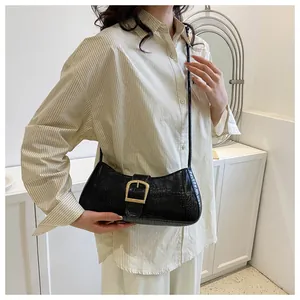 Detail of black faux leather baguette bag featuring golden buckle and crocodile pattern