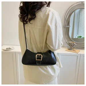 Detail of black crocodile texture baguette bag with golden buckle on female model