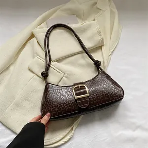 Dark brown crocodile embossed baguette bag with gold buckle on an off-white blazer