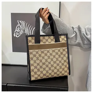 Close-up of beige tote bag with M-letter pattern and brown strap details in use