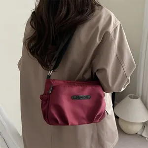 Chic burgundy pleated nylon crossbody bag worn by a model in a stylish trench coat