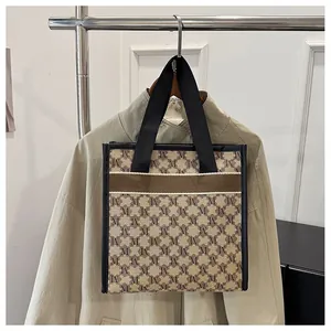 Close-up of the tote bag featuring brown M-letter monogram print and black woven handles