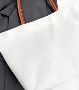 Detail of minimalist cream canvas tote bag with brown leather handles on grey fabric