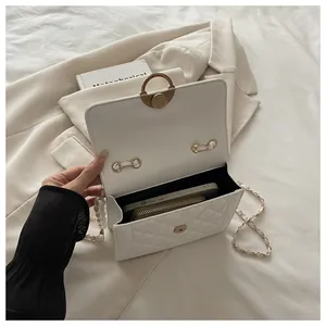 Makroansicht der weißen Stepptasche mit goldener Schnalle und eleganter Perlenverzierung