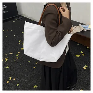 Minimalist white canvas tote bag with brown leather handles worn in an autumn street style view