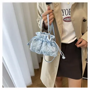 Detail of light blue quilted puff bucket bag with drawstring closure on model's shoulder