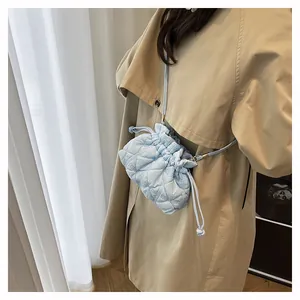 Close-up of light blue quilted drawstring bucket bag styled with a khaki trench coat