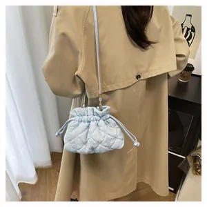 Side view of light blue quilted bucket bag with drawstring on tan trench coat