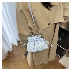 Close-up of a light blue quilted bucket bag with drawstring closure on a beige coat