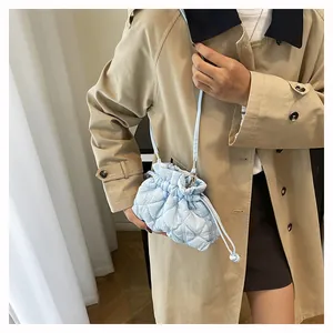 Close-up of light blue quilted drawstring bucket bag styled with a modern trench coat