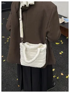 White quilted shoulder bag worn cross-body style with brown coat and autumn leaves backdrop