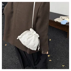 Street style view of white quilted drawstring crossbody bag with puffed texture