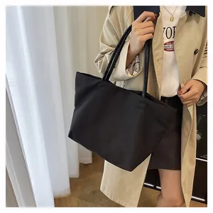 Detail of minimalist black canvas tote bag shown worn on shoulder with beige trench coat