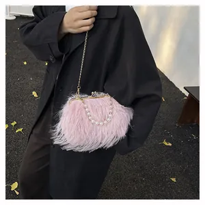 Clutch in piume rosa con manico di perle e catena dorata su un cappotto nero
