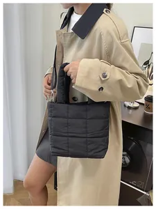 Quilted black tote bag with shoulder strap shown on a model wearing a beige trench coat