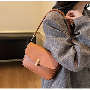 Close-up of caramel leather shoulder bag with golden metallic clasp and chain strap detail