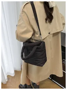 Detail of a black quilted cloud bag with wide nylon strap on a beige trench coat