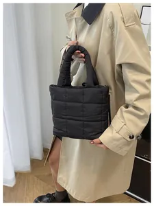 Close-up of black quilted puffer tote bag with stitched grid pattern held by model