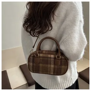 Detailed close-up of brown plaid wool handbag with leather straps worn by model