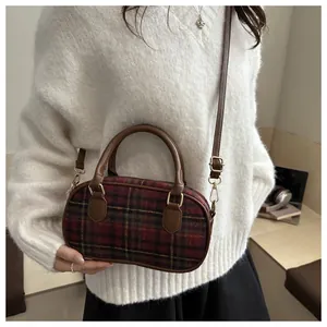 Detail of red and green plaid wool crossbody bag with brown leather trim and zipper