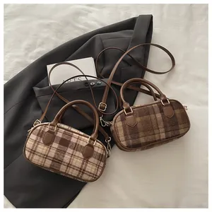 Flat lay of plaid cylinder bags with brown leather handles on a white fabric background