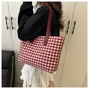 Detailed view of red and white houndstooth tote bag worn by a model in a cozy setting
