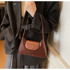 Brown crocodile pattern faux leather shoulder bag with a metal bow detail shown on a model