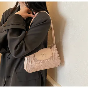 Close-up of a nude faux crocodile shoulder bag with a gold metal bow and grey blazer