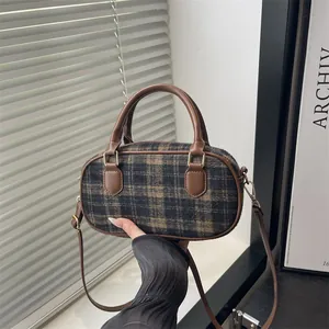 Brown plaid wool crossbody bag with leather handle shown in a stylish minimalist setting