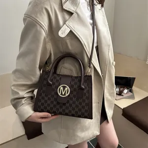 Retro brown leather handbag with 'M' print and gold logo worn by woman in office