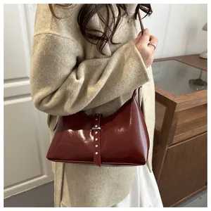 Detail view of burgundy glossy leather underarm bag with silver buckles and studs