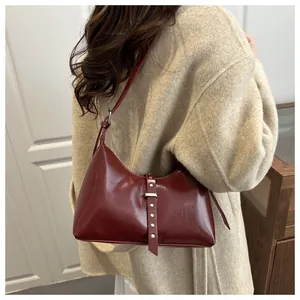 Dettaglio di una borsa a spalla vintage in pelle bordeaux abbinata a un cappotto beige